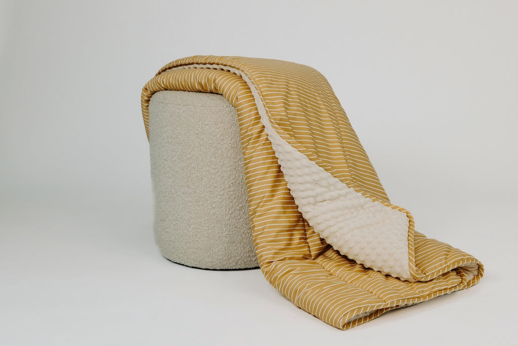Yellow striped blanket draped over stool on white background. 