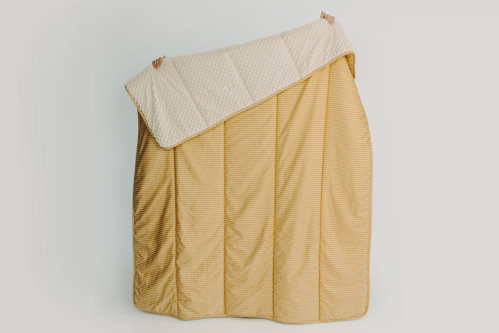 Person holding a yellow and cream blanket showing the cream minky on a white background. 