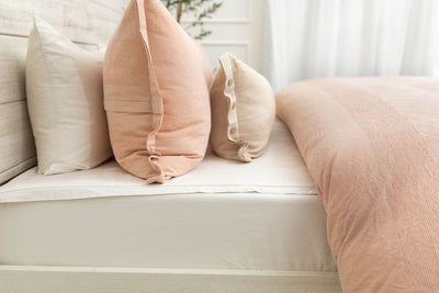 A sideview of a bed made with white zipper sheets and a peach zipper duvet folded half way down the bed and adorned with matching peach and neutral pillows.