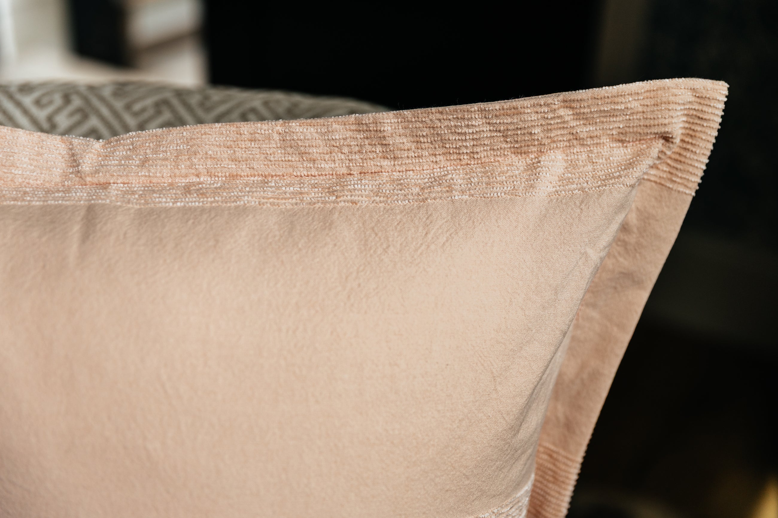 A close up corner view of a pink euro pillow with a faded striped arranged on an antique chair.