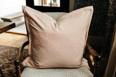 A pink euro pillow with a faded striped arranged on an antique chair by a kitchen table.