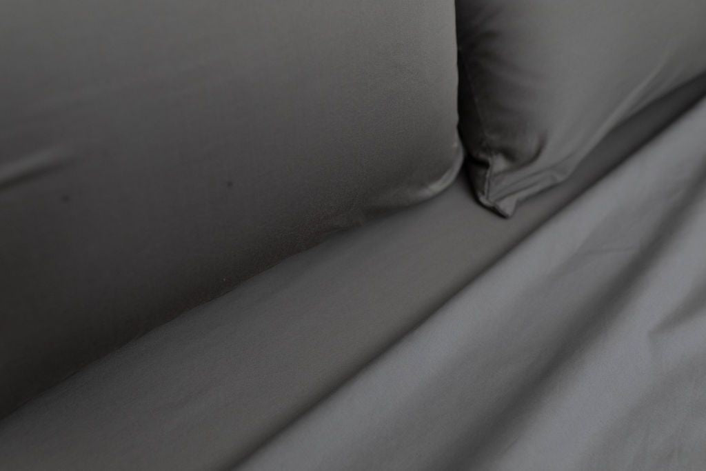 A close up view of a bed made with gray zipper sheets and matching pillows.