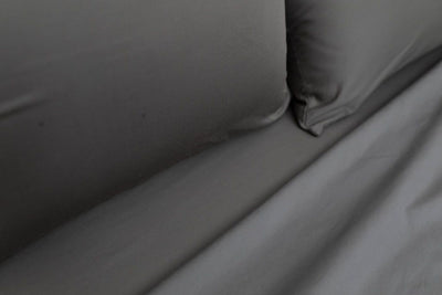 A close up view of a bed made with gray zipper sheets and matching pillows.