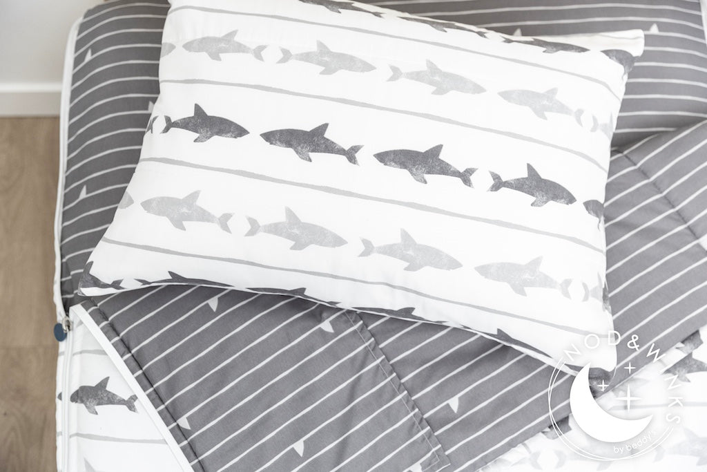 A twin bed made with shark kids zipper bedding, the top unzipped and pulled slightly back and a pillow on top
