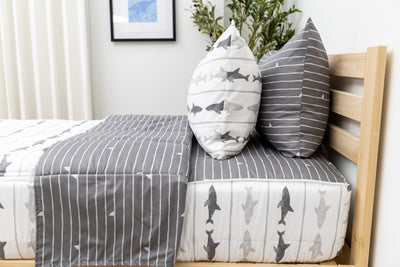 A side shot of a twin bed made with shark zipper bedding, the top unzipped and pulled slightly back and two pillows at the head of the bed