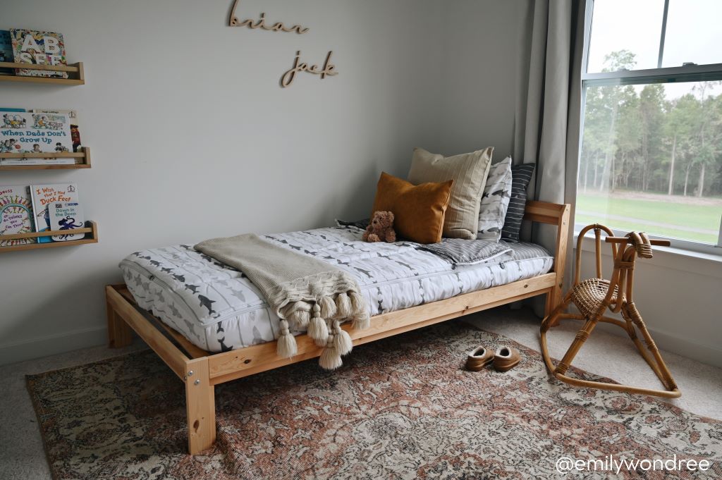 A twin bed made with shark kids zipper bedding with a wicker rocking horse beside it and floating shelves on the wall holding an assortment of books