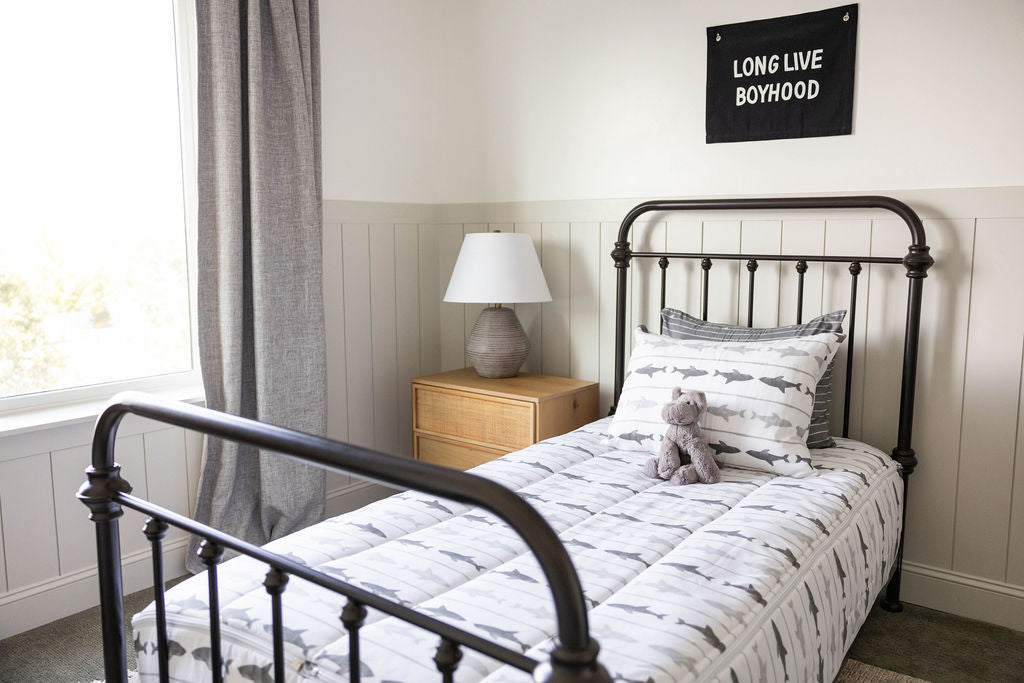 A twin bed made with shark kids zipper bedding with a nightstand beside it holding a small lamp