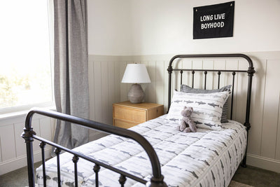 A twin bed made with shark kids zipper bedding with a nightstand beside it holding a small lamp
