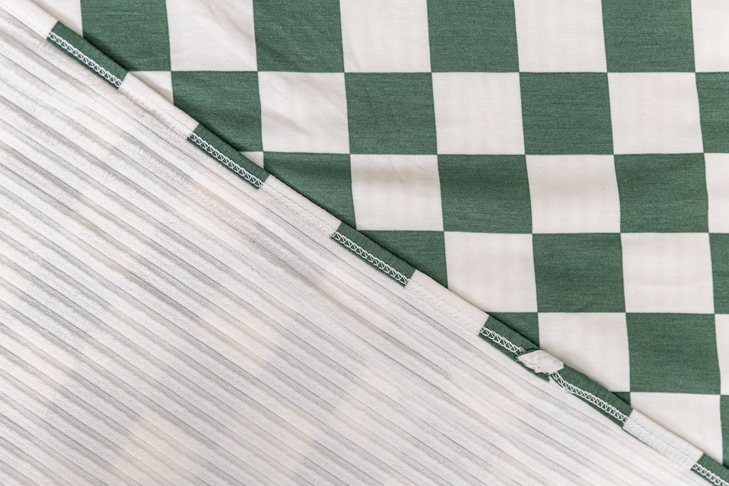 A close-up front and back view of a green check printed travel blanket. 