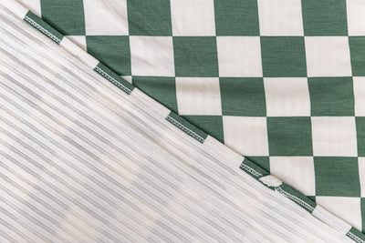 A close-up front and back view of a green check printed travel blanket. 