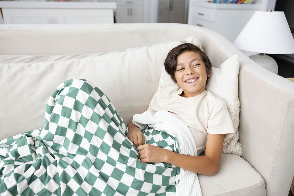 A child on a couch with a green and white checkered print blanket on them. 