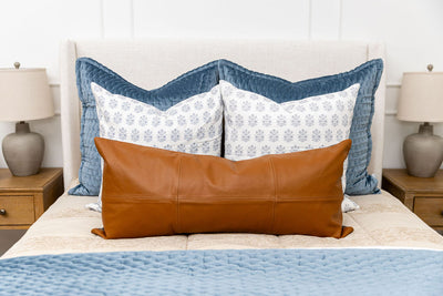A queen bed made with tan zipper bedding and an assortment of blue and leather bedding accessories