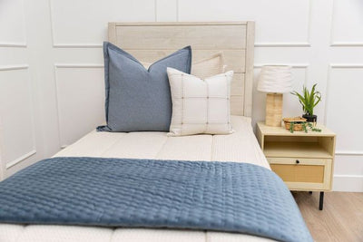 A twin bed made with cream waffle textured zipper bedding and neutral and blue pillows and blanket.