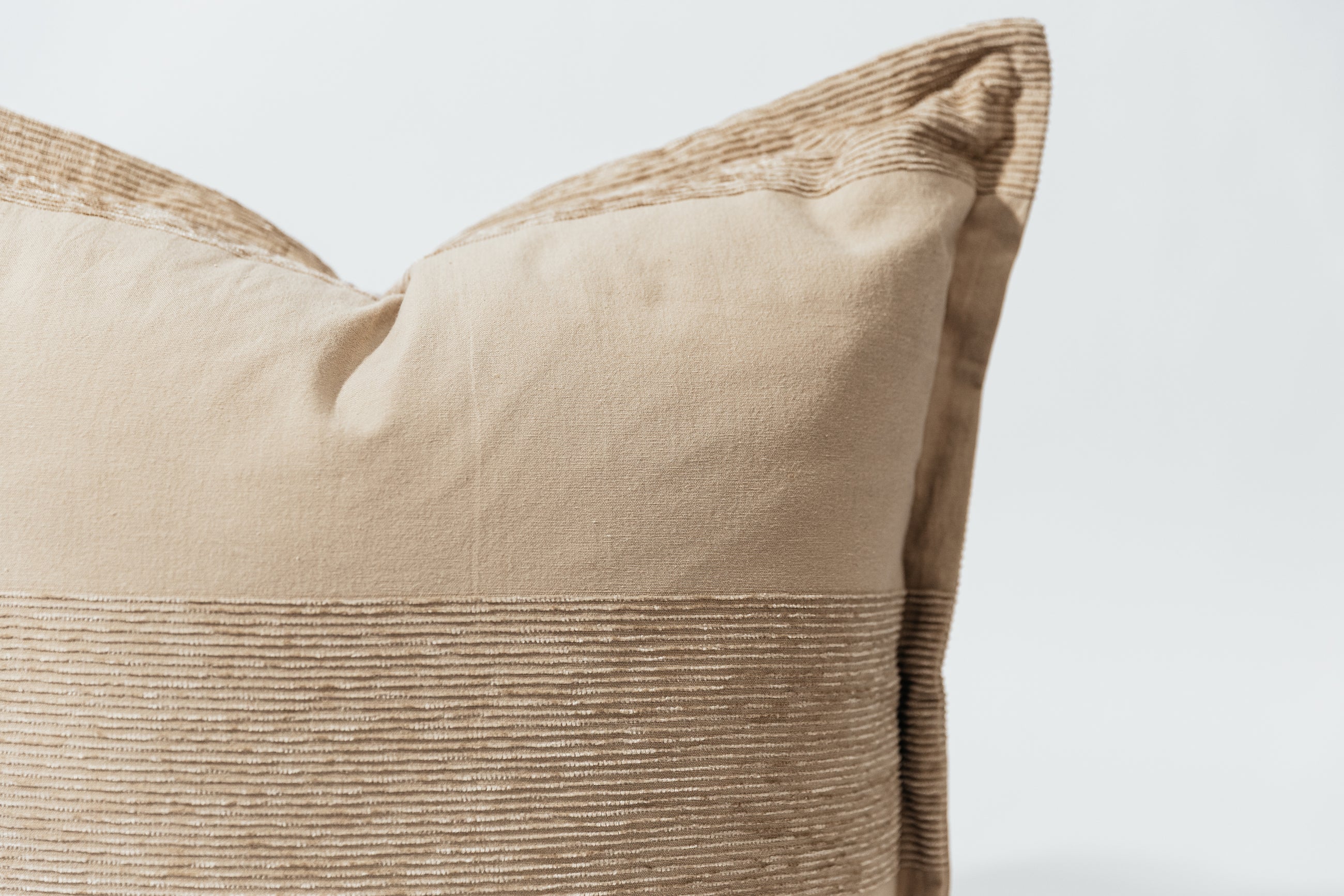 A close up corner view of a tan chenille banded stripe neutral pillow on a white background.
