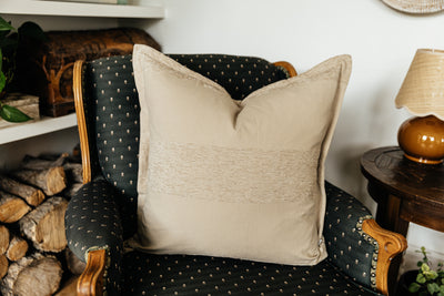 A tan chenille banded stripe neutral pillow on a black antique chair in a corner of a room.