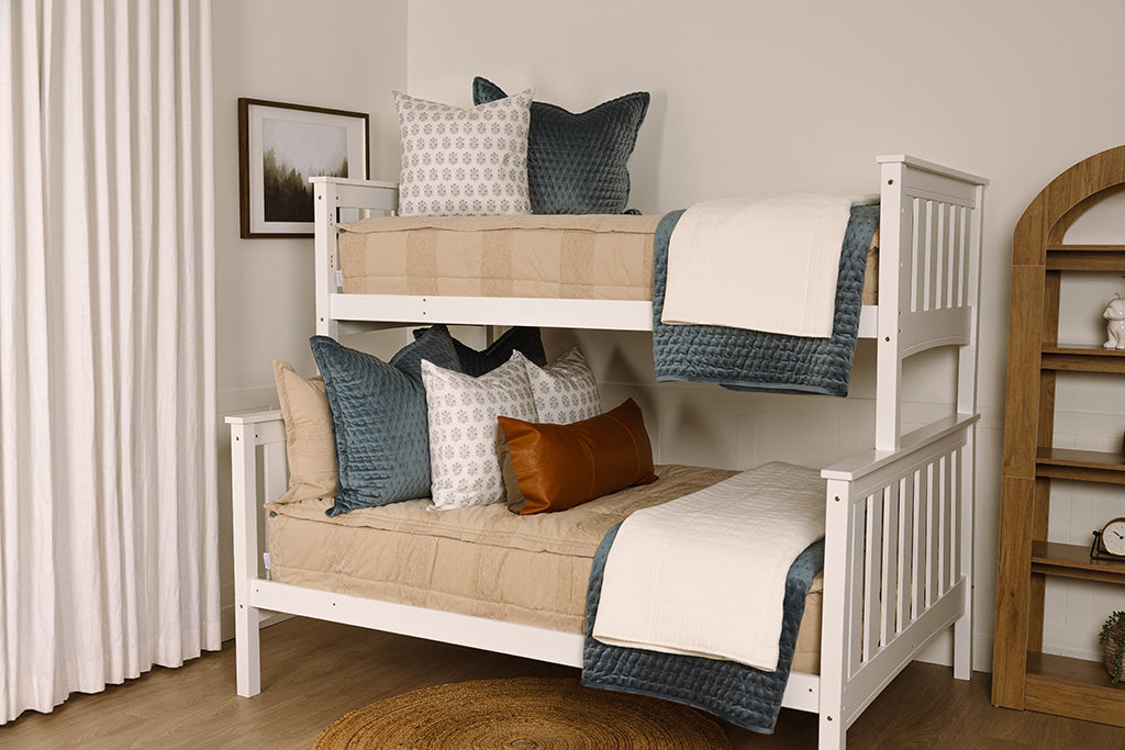 A bunk bed made with tan zipper bedding and an assortment of blue, leather, and white bedding accessories.