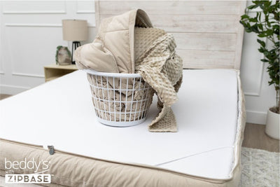 A bed made with just the fitted bedding base around the sides of the mattress, with the top comforter and ZipBase sheet in a basket on top of the bed.