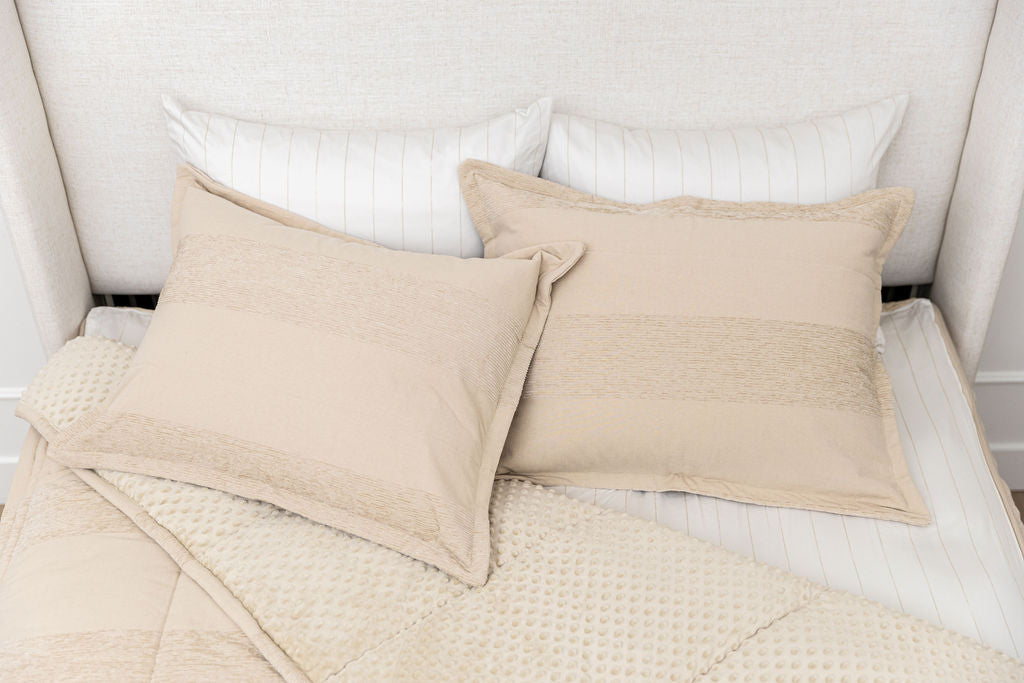 A bed made with tan faded stripes zipper bedding with the comforter pulled back and pillows on top of the bed.