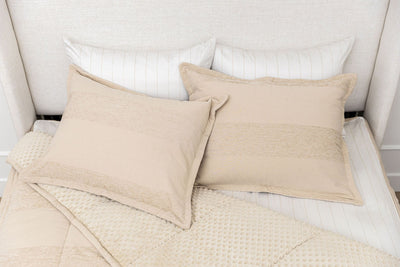 A bed made with tan faded stripes zipper bedding with the comforter pulled back and pillows on top of the bed.