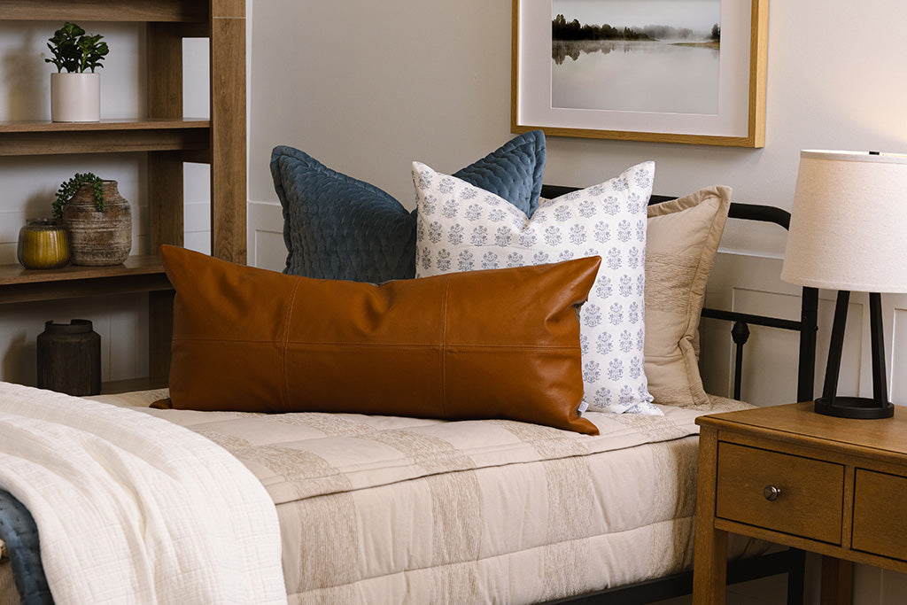 A twin bed made with tan zipper bedding and an assortment of blue, leather, and white bedding accessories