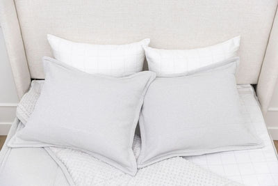 A bed made with light gray waffle textured zipper bedding with the comforter pulled back and pillows on top of the bed.