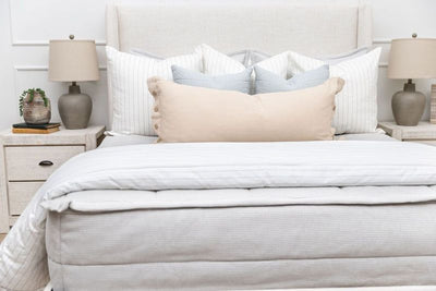A bed made with light gray waffle texture zipper bedding and an assortment of neutral and striped pillows and blanket.