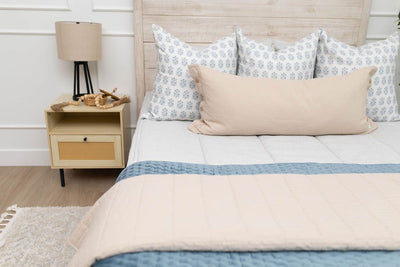 A close up view of a bed made with light gray waffle textured zipper bedding and an assortment of blue pattern and neutral pillows and blankets.