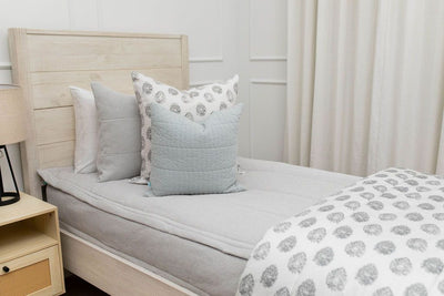 A twin bed made with light gray waffle textured zipper bedding and an assortment of blue and gray pattern pillows and blanket.