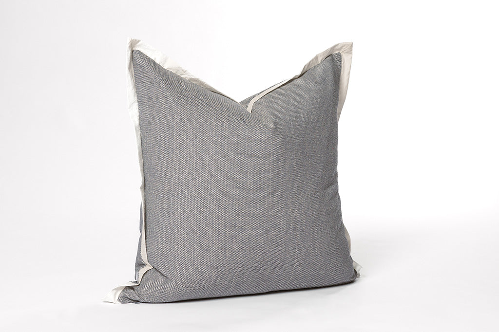 Blue pillow with white trim on a white backdrop.