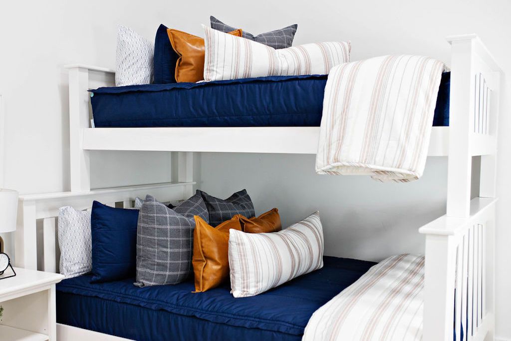 Queen bed with Navy blue zipper bedding with faux leather pillows, white XL lumbar with navy vertical stripes, and white blanket with vertical navy stripes at the foot of the bed