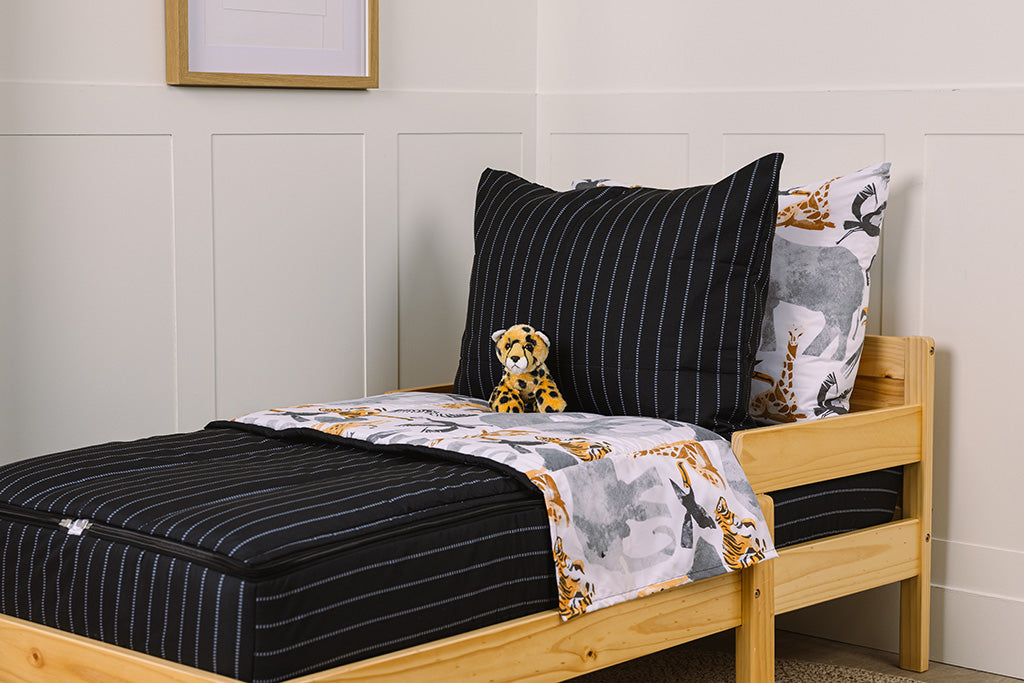 A wooden toddler bed made with black and jungle animal printed zipper bedding and a stuffed animal leaning against the pillows.