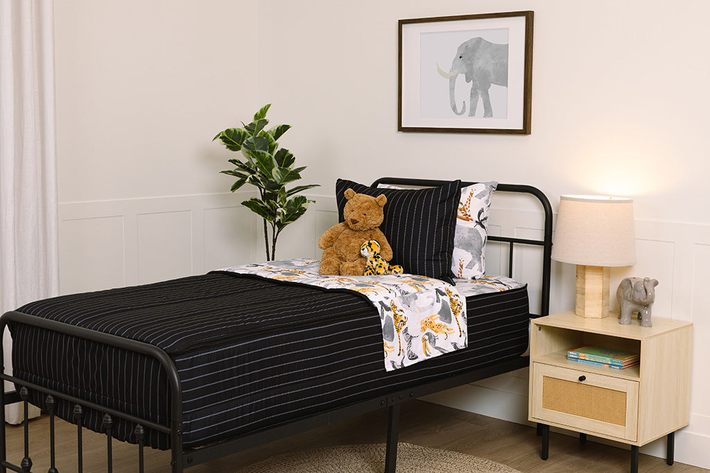 Children's zipper bedding in a bedroom on a black bed frame that has a black exterior and animal print interior, with a stuffed teddy bear and stuffed, toy cheetah. 