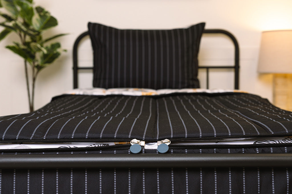 A shot of the two zippers on a set black and jungle printed zipper bedding, the zippers completely unzipped to show how they meet at the foot of the bed.