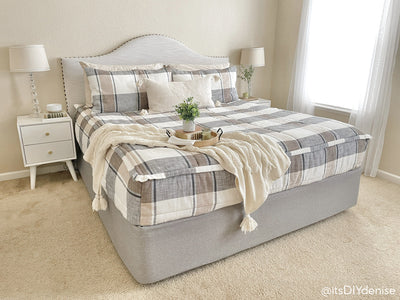 A bed made with charcoal, tan, and cream plaid zipper bedding and a neutral pillow and throw blanket.