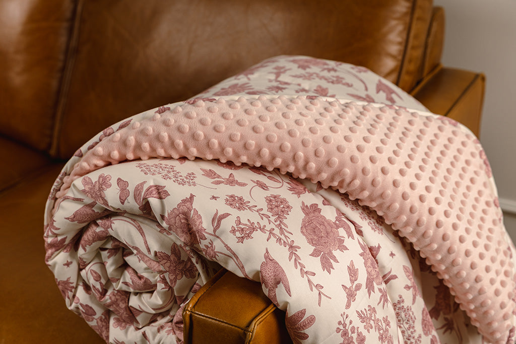A pink and white floral print and minky blanket, laying on the side of the sofa. 
