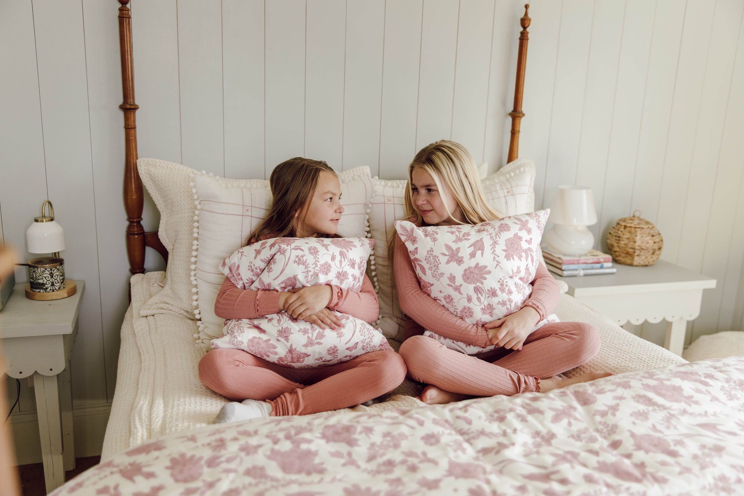 Two girls hugging pink and white pillows on cream zipper bedding