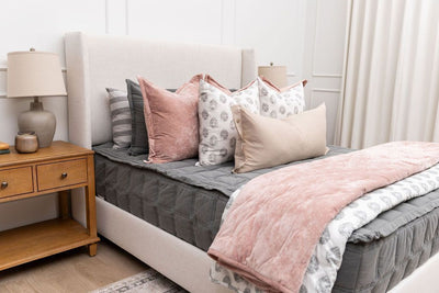 A bed made with gray zipper bedding and decorated with an assortment of floral and pink bedding accessories