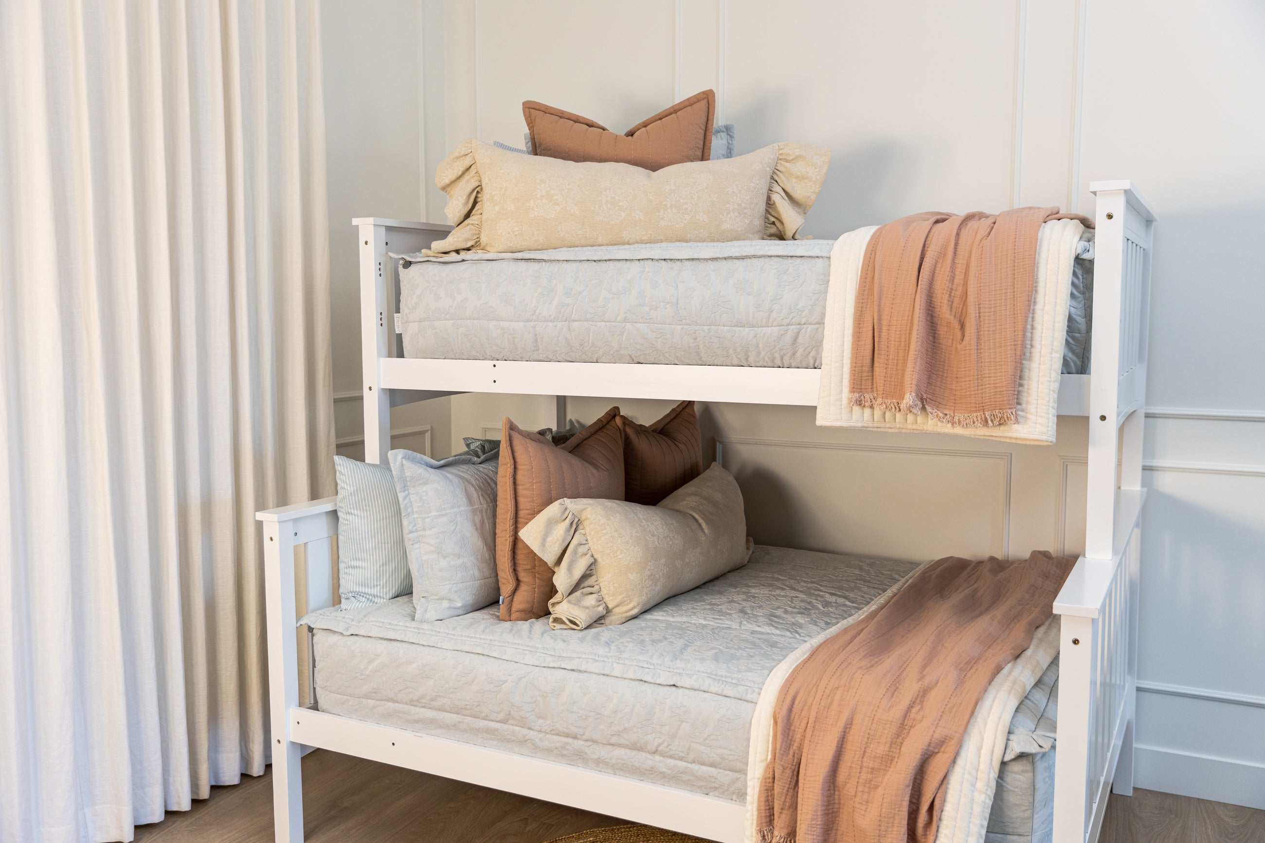 A bunk bed made with light blue zipper bedding with cream and terracotta accessories.