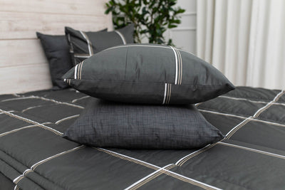 A pillowcase and matching sham on a made bed with charcoal, white and tan plaid zipper bedding. 