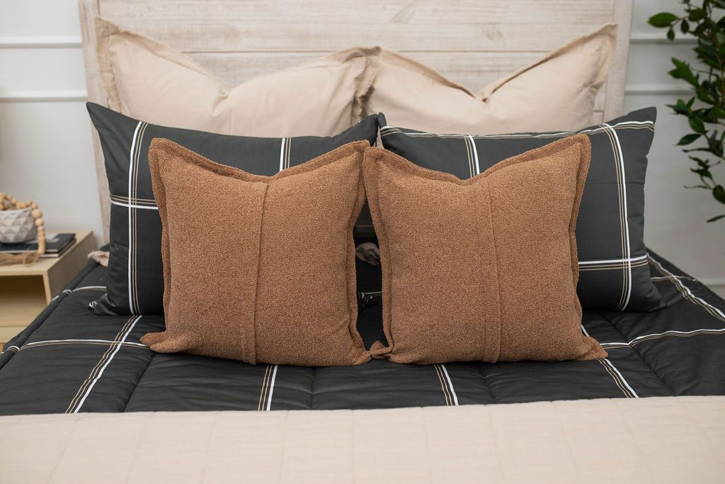A close up of the neutral brown throw pillows on a set of black plaid zipper bedding