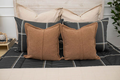 A close up of the neutral brown throw pillows on a set of black plaid zipper bedding