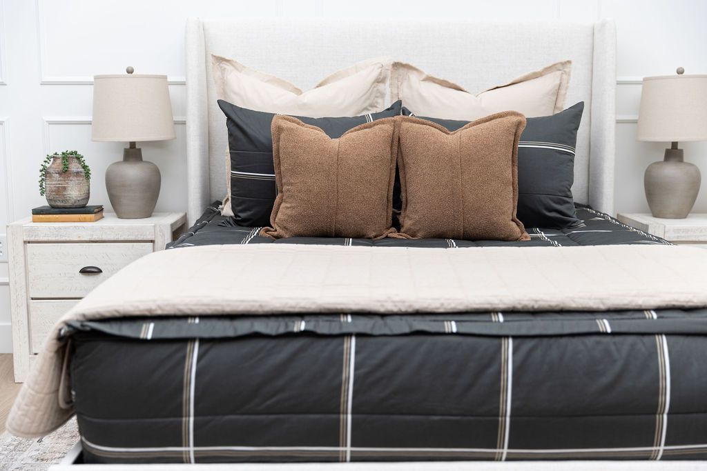 A queen bed made with black plaid zipper bedding and an assortment of neutral bedding accessories