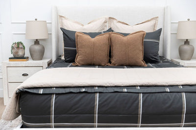 A queen bed made with black plaid zipper bedding and an assortment of neutral bedding accessories