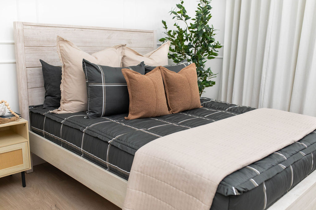 Charcoal with white and brown grid pattern bedding with tan and brown pillows and tan patterned blanket.
