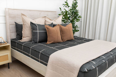 Charcoal with white and brown grid pattern bedding with tan and brown pillows and tan patterned blanket.