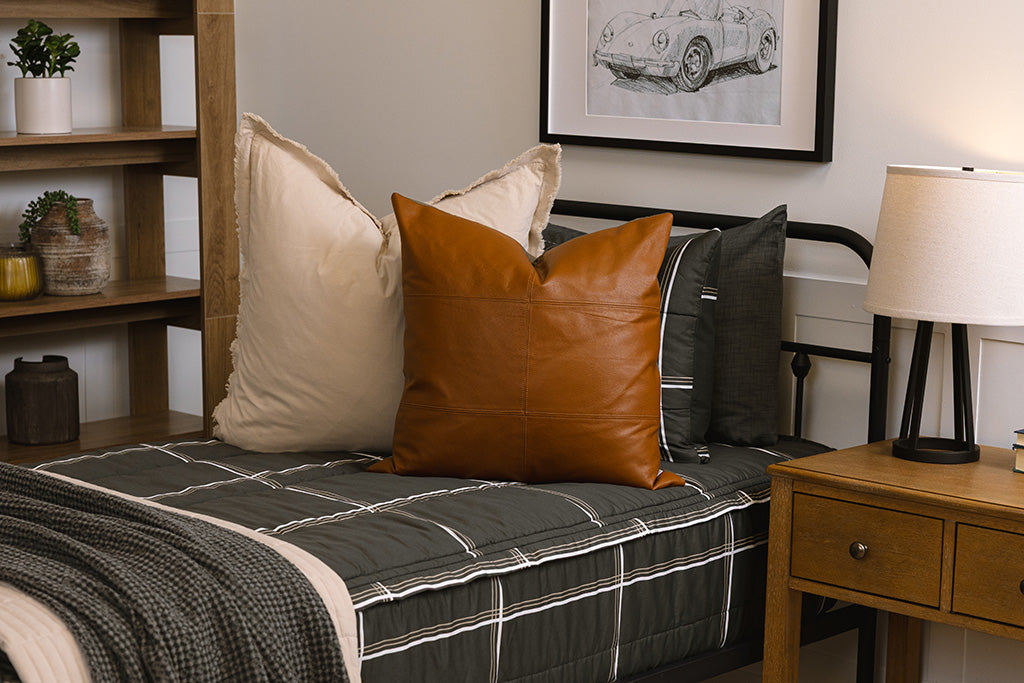 A twin bed made with charcoal with white and brown grid pattern bedding with tan and white pillows and gray throw blanket. 