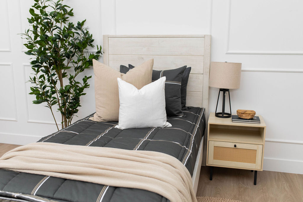A twin bed made with charcoal with white and brown grid pattern bedding with tan and white pillows and tan throw blanket. 