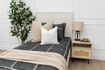 A twin bed made with charcoal with white and brown grid pattern bedding with tan and white pillows and tan throw blanket. 