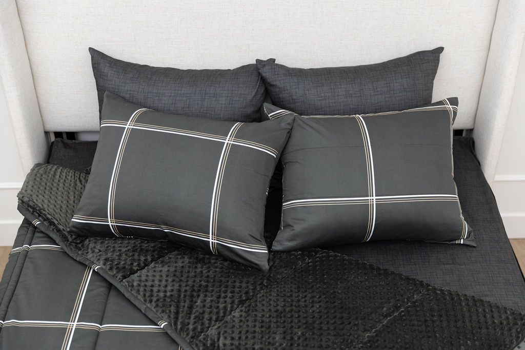 A queen bed made with black plaid zipper bedding with the top portion unzipped and slightly pulled back and four pillows arranged on top
