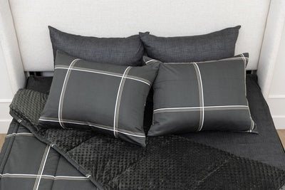 A queen bed made with black plaid zipper bedding with the top portion unzipped and slightly pulled back and four pillows arranged on top